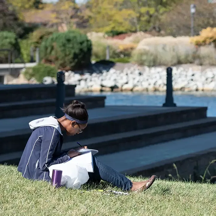 女子坐在防弹少年团台阶旁的草地上，在纸笔记本上写字.